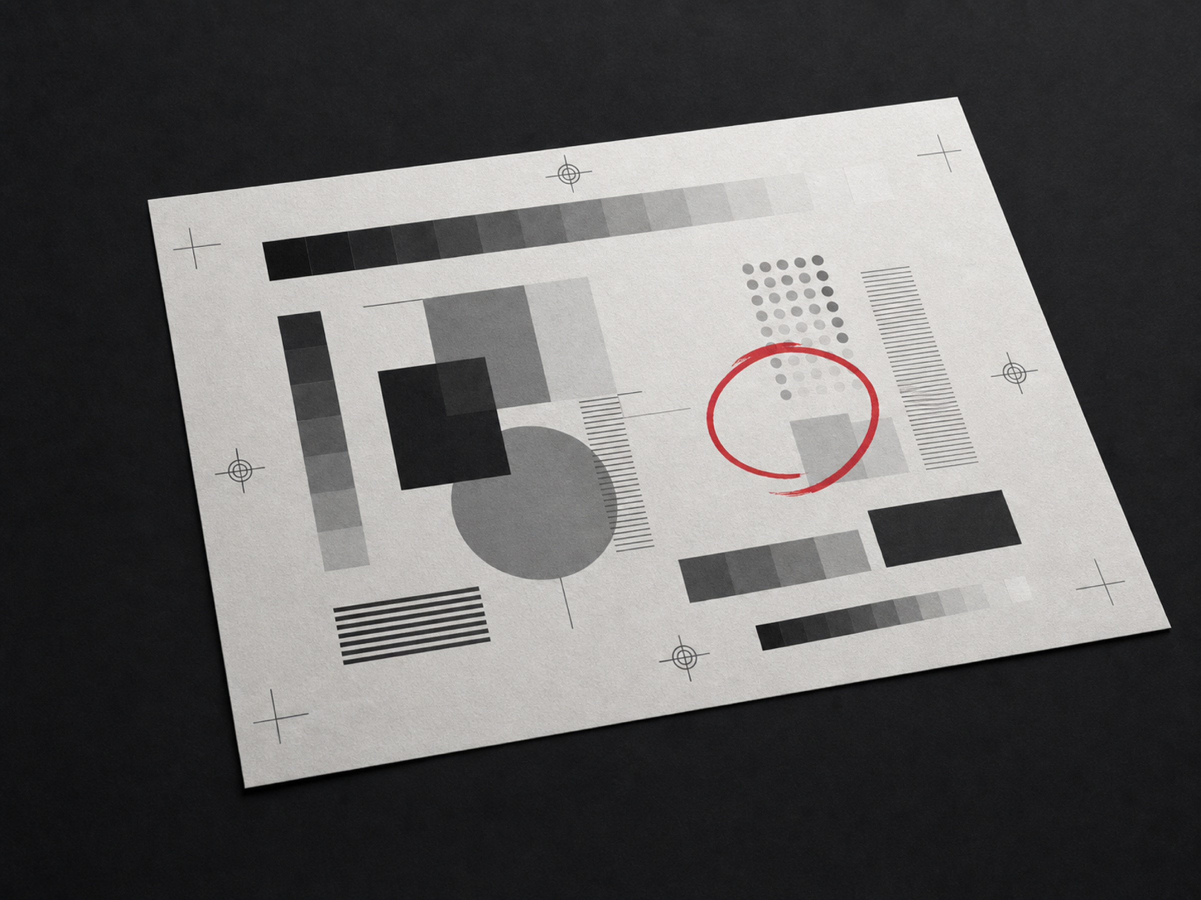A printed proof sheet on a dark surface showing greyscale test patches, tint blocks and registration marks, with one element circled in red.