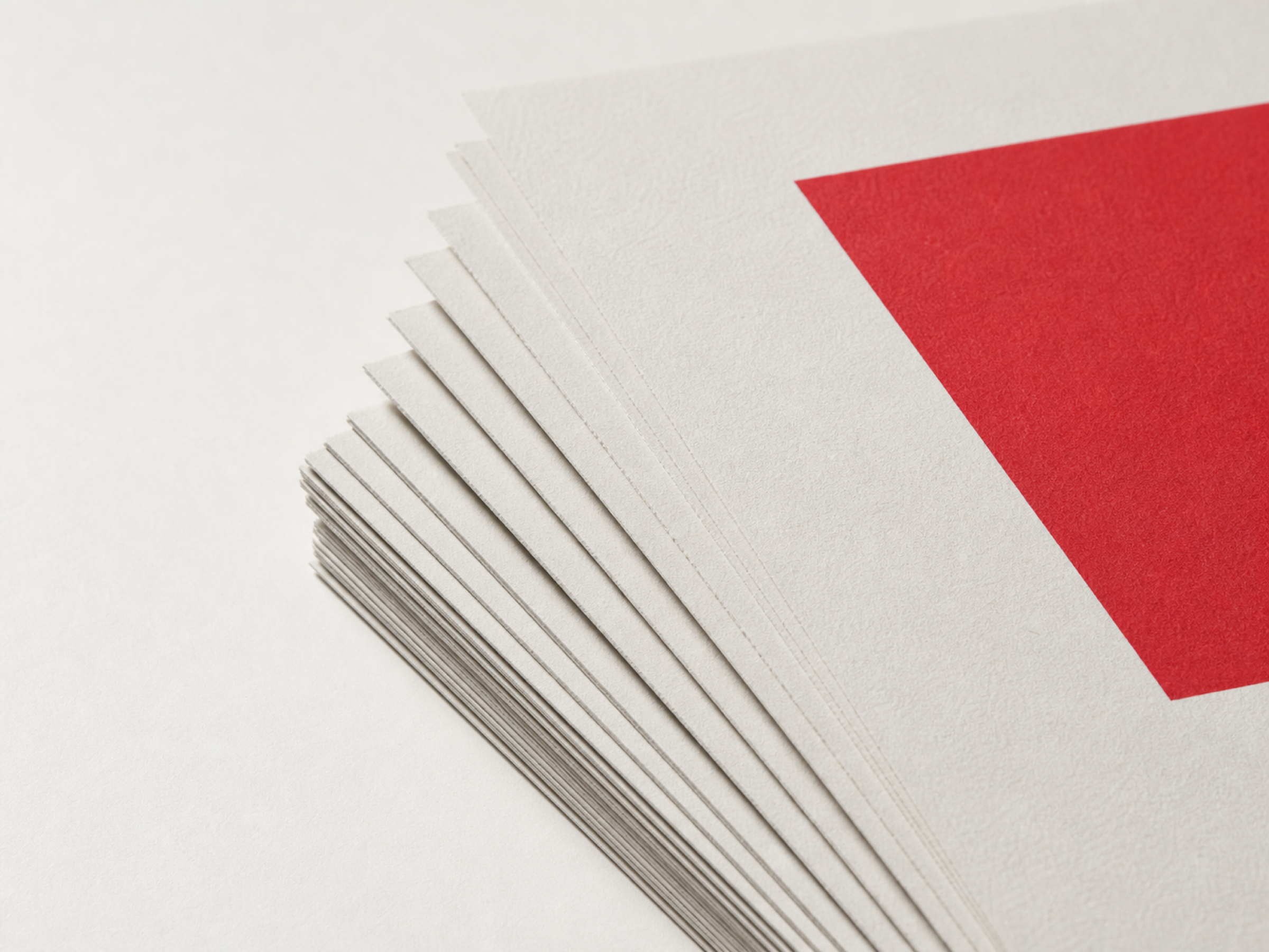A fanned stack of uncoated white sheets on a pale surface, cut edges visible, with a large solid red shape printed across the top sheet.